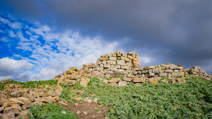 Prehistoric nuraghe stone structure rising from green landscape under dramatic sky in Sardinia