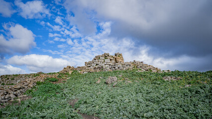 Prehistoric nuraghe stone structure rising from green landscape under dramatic sky in Sardinia