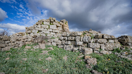 Prehistoric nuraghe stone structure rising from green landscape under dramatic sky in Sardinia