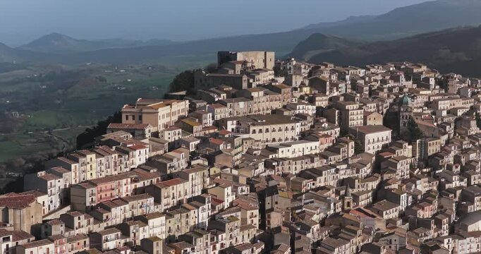 Aerial view of the ancient town with clustered buildings, a prominent castle overlooking the valley and green hills, Gangi, Sicily, Italy.