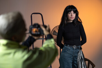 A photographer takes a picture of a young brunette woman in a photo studio. The woman is cheerful and smiling.