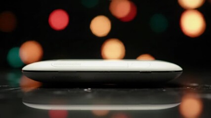 Pristine, sleek, minimalist product on polished black marble with pulsing crimson, orange, gold, teal bokeh lights. Slow tracking video, high-end celebration