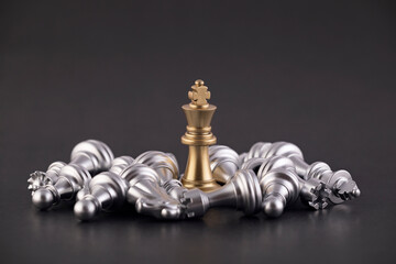 Victorious golden king with group of lying silver chess pieces