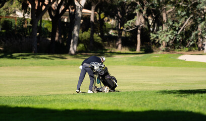 Golfer carrying clubs in his golf bag on a lush green golf course under a clear blue sky on a sunny day, enjoying the outdoors and sport.