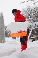 A man in an orange tracksuit clears snow from the paths near the house. An orange snow shovel.