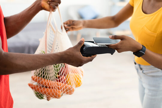 Grocery Shopping Delivery. African American Woman Paying With Credit Card For Groceries Shopper Bag Receiving Parcel With Food Products From Supermarket Courier At Home. Cropped, Selective Focus