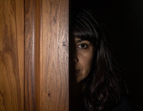 Persona adulta parcialmente visible detr&aacute;s de una puerta entreabierta, interior oscuro