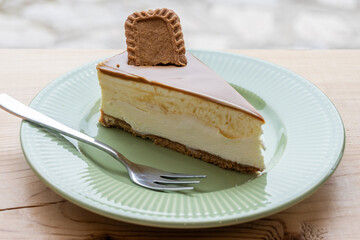 A decadent slice of creamy cheesecake topped with caramel and a biscuit, presented on a ridged green plate with a fork.