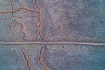Military defense fortifications along rural dirt road featuring reinforced trenches and tactical checkpoint position aerial top down view