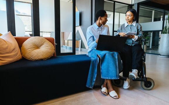 Two young women discussing work together in a modern office setting - Powered by Adobe