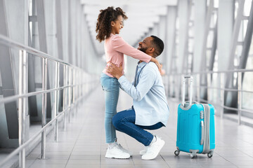 Meet And Greet Concept. Teenage black girl embracing her happy father after arrival in airport, returning back home from vacation journey voyage, smiling man hugging daughter, looking at each other