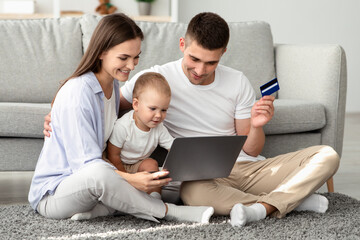 Fototapeta premium Online Shopping. Happy Parents And Their Cute Toddler Baby Using Laptop And Credit Card At Home, Young Family Of Three With And Infant Child Purchasing Things In Internet Together, Closeup Shot