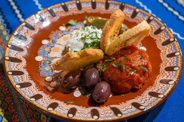 A close-up of Bulgarian appetizers featuring creamy white dip, lutenitsa (red pepper spread), olives, and toasted bread on a colorful patterned plate in Bansko, Bulgaria.