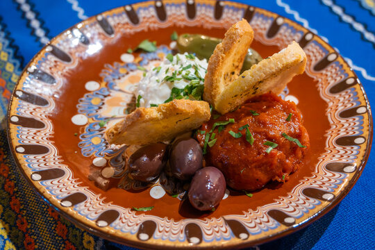 A close-up of Bulgarian appetizers featuring creamy white dip, lutenitsa (red pepper spread), olives, and toasted bread on a colorful patterned plate in Bansko, Bulgaria.