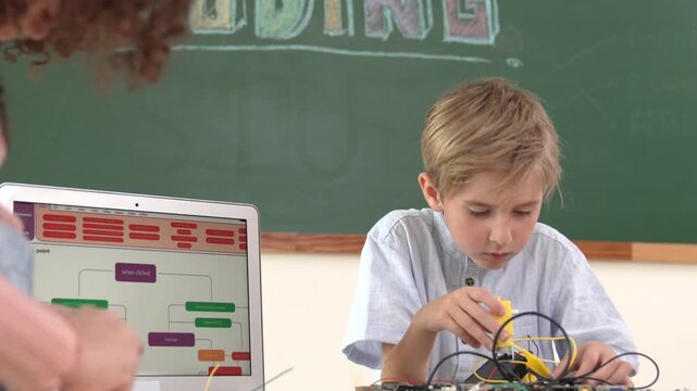 Caucasian smart boy fixing main board by using screwdriver at stem technology lesson while smiling student working together to inspect electronic machine at table with laptop display code. Pedagogy.