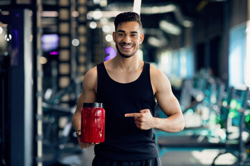 Bodybuilding Nutrition. Happy Arab Sportsman Pointing At Red Container With Whey Powder While...