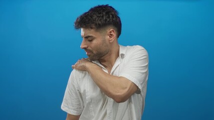 Hispanic young man with hand on shoulder in studio wearing white linen shirt and trimmed beard; discomfort.