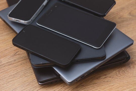 Stack smartphones, tablets, and laptops on a wooden table, showcasing modern digital devices. Concept technology abundance, multitasking, gadget collection and contemporary digital lifestyle.