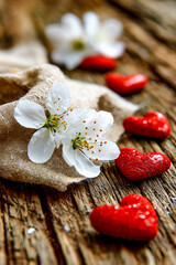 White cherry blossoms and red heart shapes on aged wooden planks background.