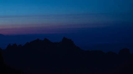 Dark mountain range silhouette against a deep twilight sky exhibiting vibrant gradients of indigo blue and subtle magenta horizon bands during the transition from night to morning