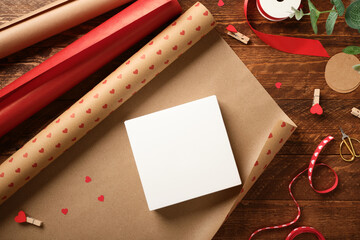 Unpacked box lies on wrapping paper. Around it are ribbon, scissors, tape, and small hearts. Preparing for the holidays.