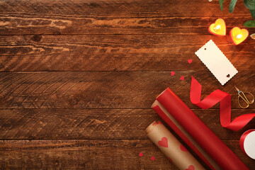Wrapping rolls, red ribbon, label, and heart candles on wooden background. Valentine's Day or romantic evening concept. Copy space.
