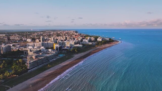 Aerial view of Jo&atilde;o Pessoa coastline in Para&iacute;ba, Brazil, showing turquoise ocean, urban skyline, sandy beaches, and tropical city landscape under clear blue sky.