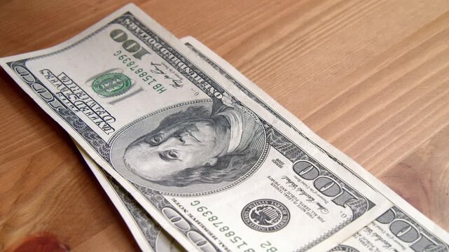 Close Up Shot Of A Pile Of One Hundred Dollar Banknotes Dropped On A Wooden Table In Slow Motion. Finance Money Wealth Banking And Investment Concept.