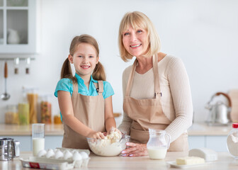 Portrait of smiling caucasian granny and small granddaughter having fun cooking at home kitchen...