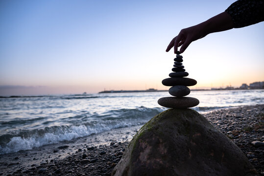 A girl's hand stacks stones into a pyramid on the beach