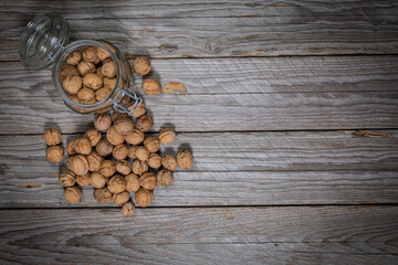 Top-down studio shot of whole walnuts and an open glass jar on weathered wooden boards
