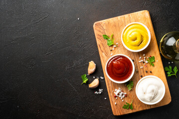 Ketchup, mayonnaise and mustard in the bowls on black background.