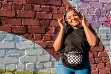 African american woman dancing playfully with headphones against painted wall. Concept of joy, energy, fun and youth lifestyle.