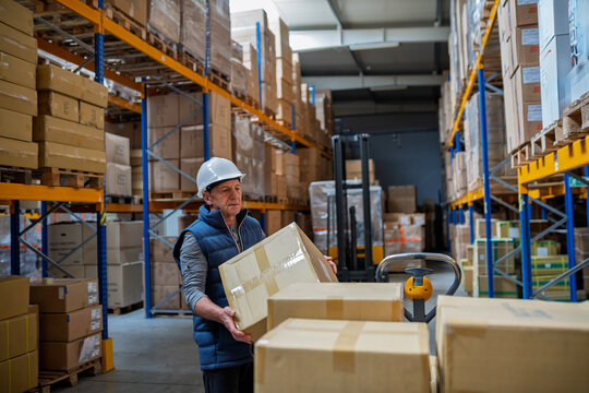 Older male warehouse worker pulling a pallet truck.