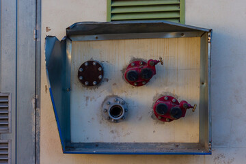 Industrial Wall-Mounted Valve Box With Red Handles And Weathered Metal Surface Outdoors
