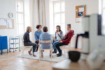 Group of people sitting in a circle and sharing experiences during guided therapeutic session.