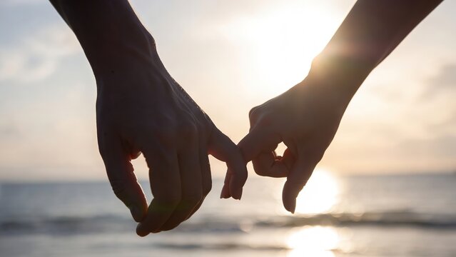 Two hands make a sweet pinky promise, fingers gently interlocked against the breathtaking, blurred backdrop of a warm sunset over the tranquil ocean.