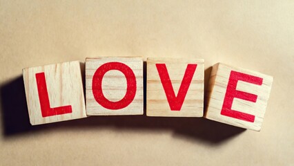 Four rustic wooden blocks with red letters spell "LOVE" against a warm textured beige background.