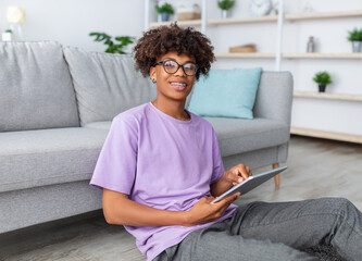 Positive black teen guy in casual wear having online lesson on tablet pc at home. African American...