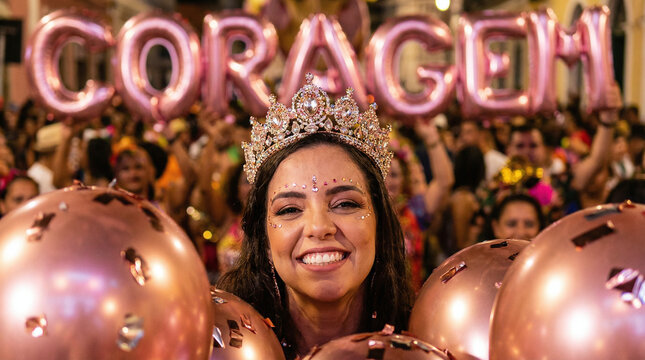 a smiling woman with dark hair, wearing a sparkly tiara, surrounded by pink balloons and a crowd. Large pink "CORAZ&Oacute;N" balloons in background. Bright, festive setting.