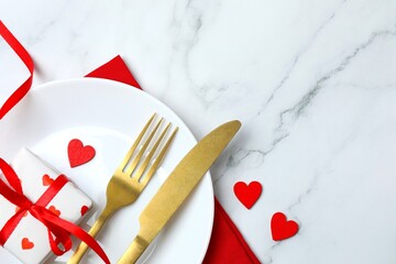 Valentine's Day. Top view photo with plate, cutlery, gift box, red hearts on marble background with...