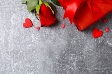 Beautiful red rose, gift box and hearts on gray background