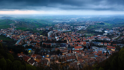 Panoramic view of a Republic San Marino, Italy. A wide, panoramic, high-angle view of a historic European town with terracotta roofs in a lush green valley.  