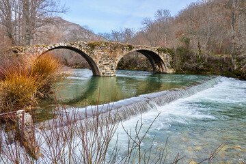 Ancient stone bridge with waterfall in forest landscape