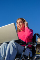 Young woman in wheelchair using laptop and headphones