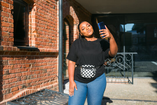 Woman taking selfie with smartphone near brick building. Personal expression, digital communication, and social media storytelling through mobile photography and lifestyle branding