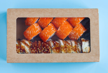 Craft paper package with mixed sushi set. Japanese cuisine delivery container with salmon and eel rolls. Flat lay of Asian dinner meal on light surface. Photo