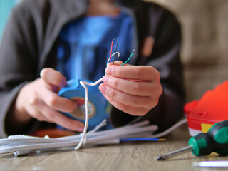Child's Hands Repairing a White Electrical Cord with Blue Tape - Learning Technical Skills: A Young Person Working with Exposed Electrical Wires
