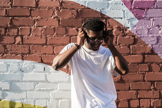 Man dancing happily with headphones by colorful wall. Positive mood, music therapy, and carefree lifestyle through urban street performance - Powered by Adobe