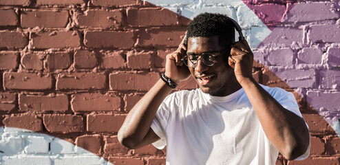 Man dancing happily with headphones by colorful wall. Positive mood, music therapy, and carefree lifestyle through urban street performance